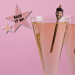 Two glasses of pink liquid with novelty straws featuring faces on a pink background with 'Bach It Up!' text.