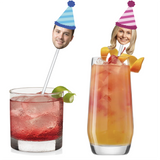 cut outs of a male and female's faces wearing matching striped party hats in blue stripes and pink stripes on a drink stir stick in cocktail glasses