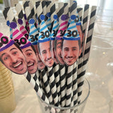 Straws with faces and '30' hats in a glass on a white surface