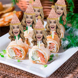 blond woman wearing a glitter pink party hat on a clear cocktail pick stuck into pinwheel appetizers