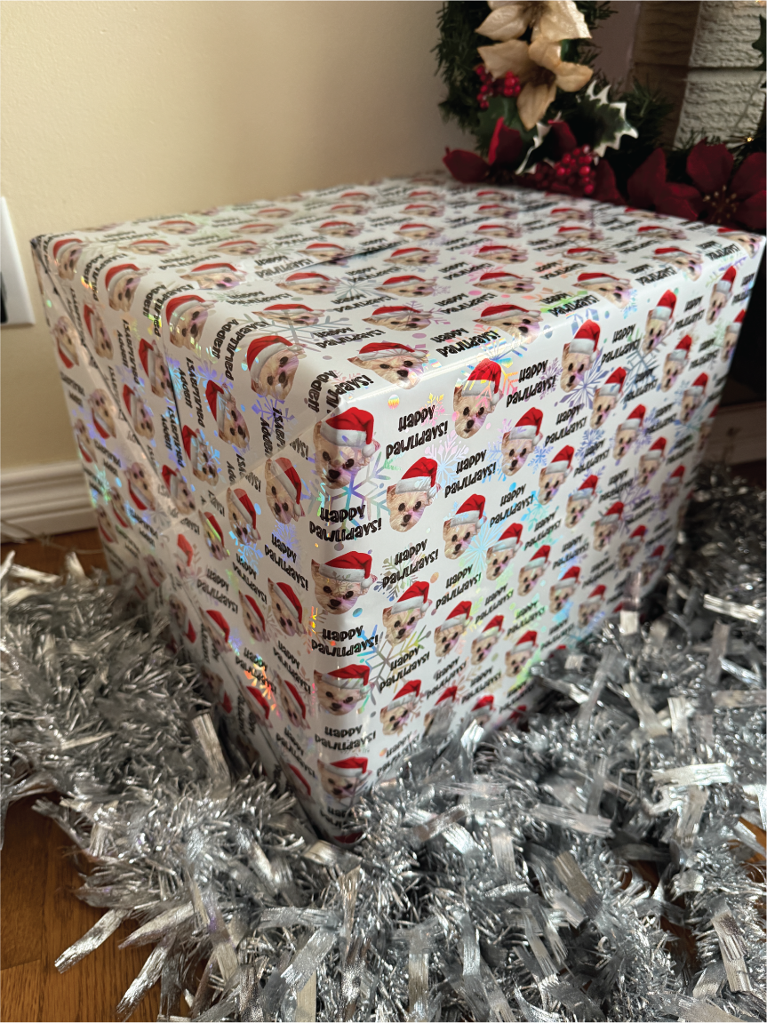 Cube-shaped gift box wrapped in festive paper with dogs face wearing santa hat and happy pawlidays, surrounded by tinsel.