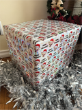 Cube-shaped gift box wrapped in festive paper with dogs face wearing santa hat and happy pawlidays, surrounded by tinsel.
