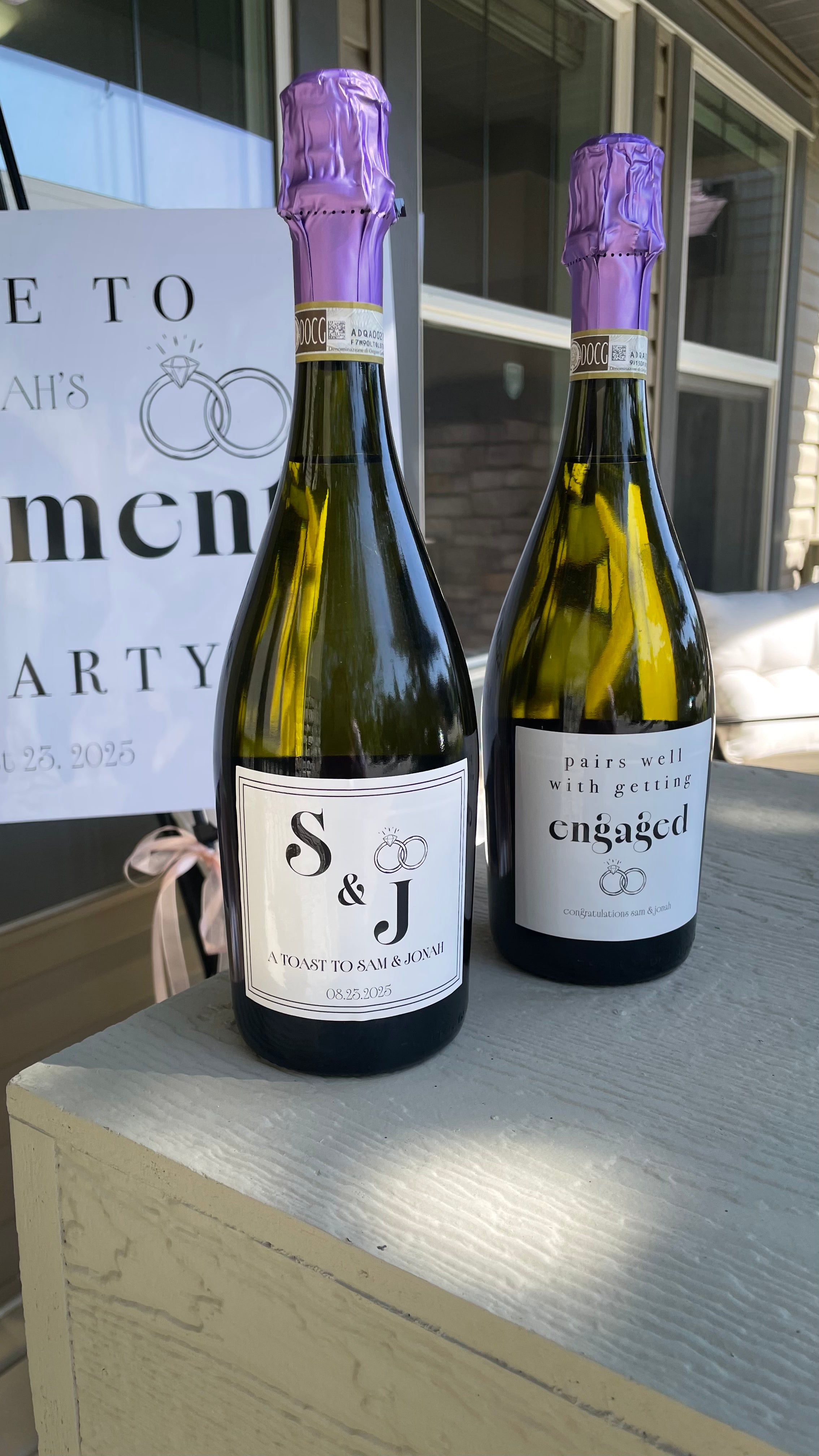 Two bottles of S&J wine with purple corks on a wooden surface, with a blurred background.