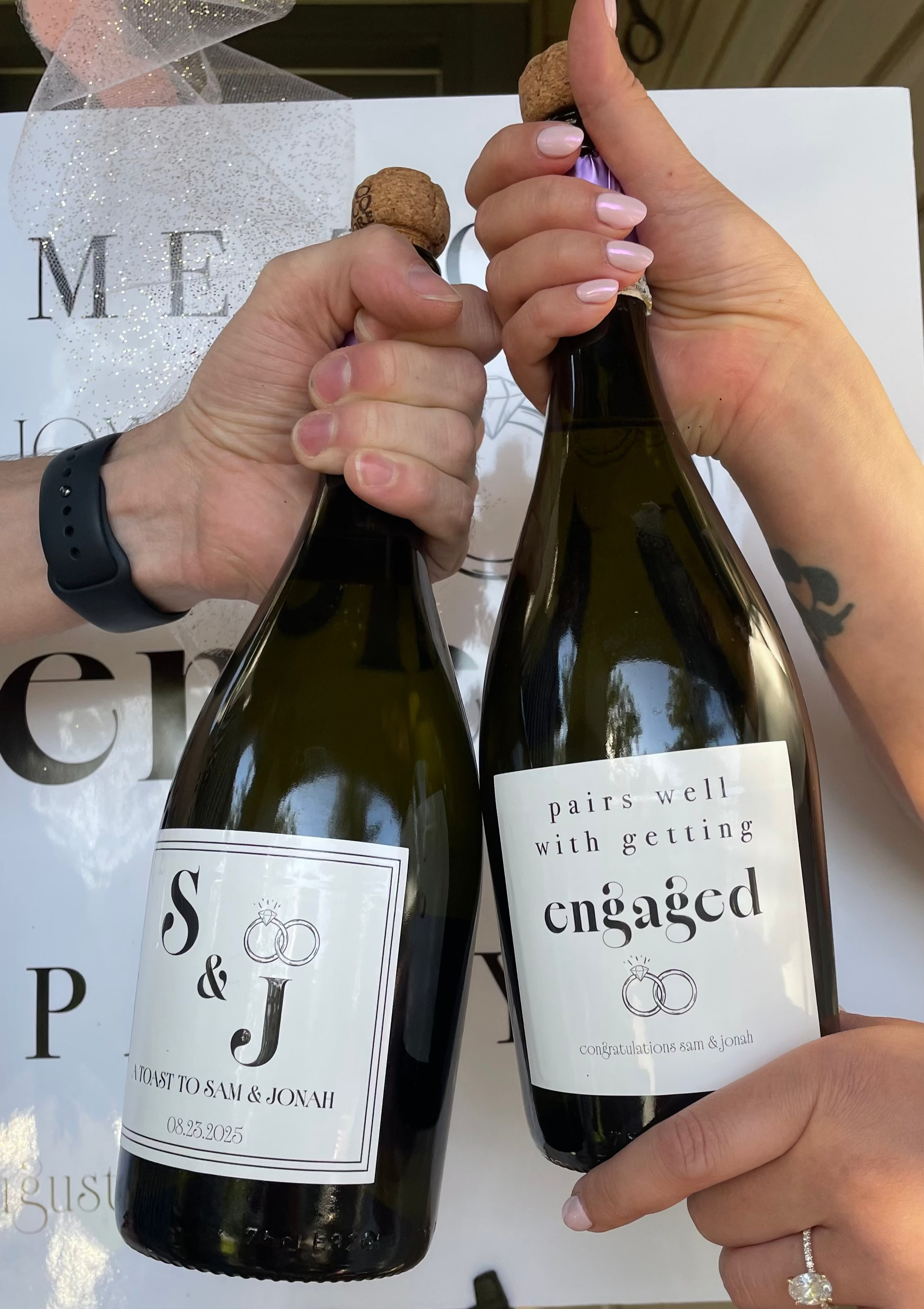 Two bottles of wine held by hands with a 'engaged' label, against a blurred background.