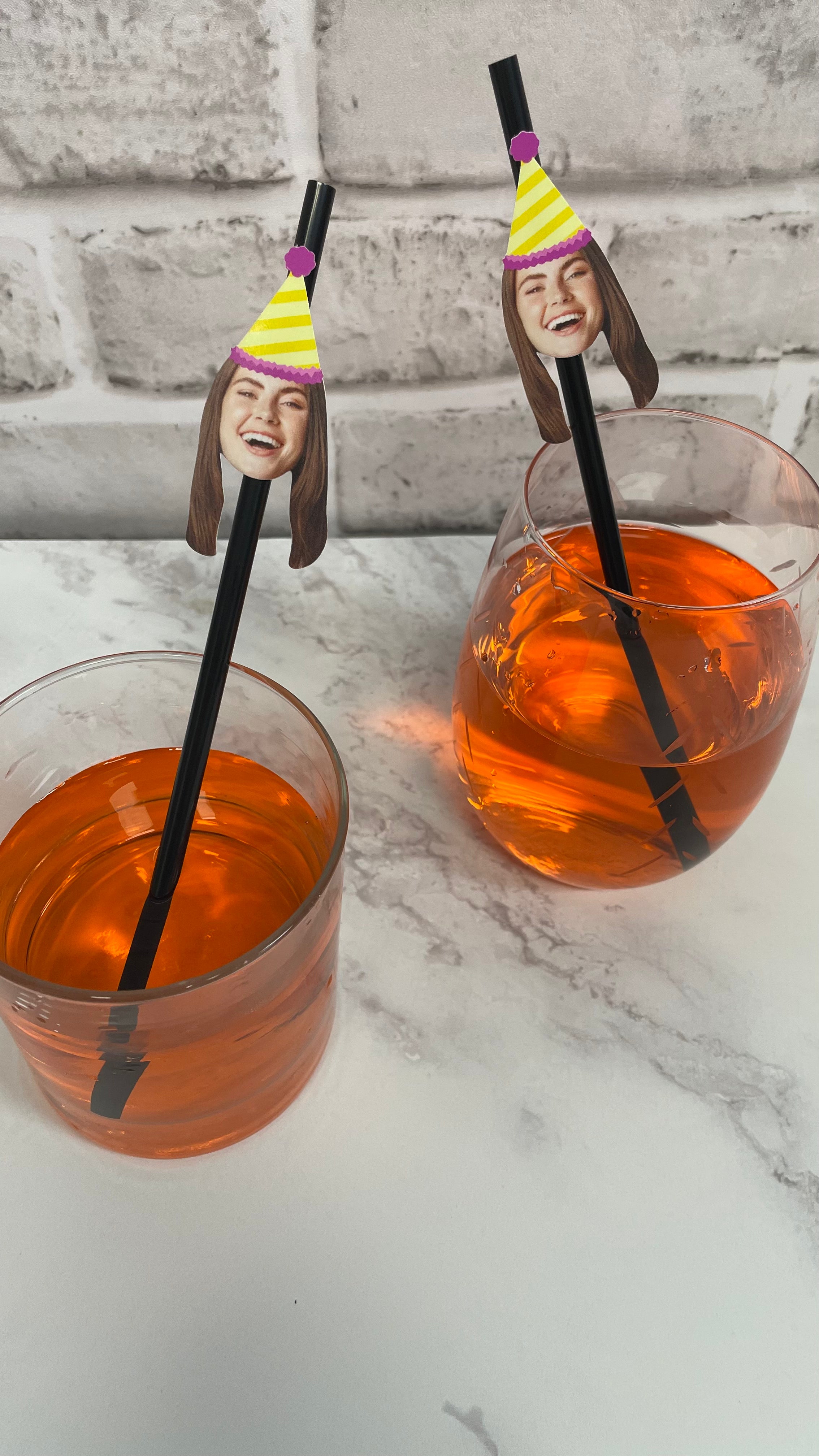 Two glasses of orange liquid with straws featuring faces on a marble surface.