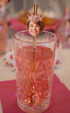 Glass of pink drink with a straw featuring a photo of a smiling person wearing a 'Bride' tiara.