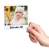 Hand holding a photo card with a baby in a bear hat and scarf, surrounded by autumn leaves, with text 'Look who's 40!'.