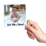 Hand holding a card with a baby photo and 'Look Who's Retired!' text against a white background