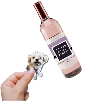 Wine bottle with personalized label and a small dog sticker held by a hand on a white background