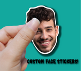 Hand holding a custom face sticker of a smiling person against a teal background