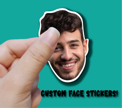 Hand holding a custom face sticker of a smiling person against a teal background