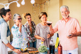 an older group of people surrounding a food and drink table at a party
