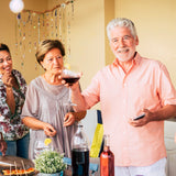 3 people at a party gathered around a food table and the man in front is holding up a glass of red wine