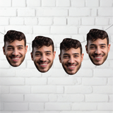 Four cardboard cutouts of a smiling man's face against a white brick wall background.